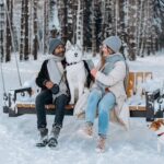 Woman in White Jacket Sitting on Brown Wooden Bench Beside White and Brown Dog on Snow