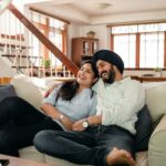 Happy young Indian couple laughing and cuddling while relaxing on couch