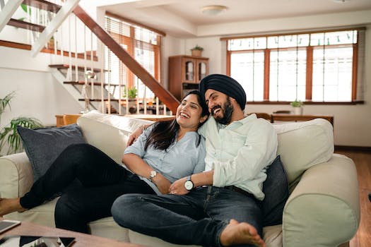 Happy young Indian couple laughing and cuddling while relaxing on couch
