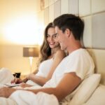 Smiling young couple browsing laptop together on bed