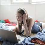 Young woman watching movie in headphones in messy room