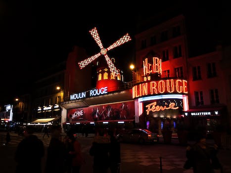 Exterior of famous cabaret club with glowing neon light illumination and banners decorate with luminous mill and located on street of Paris at night