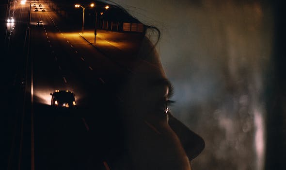 Side view crop female sitting in car behind window glass reflecting road with moving cars and street lights at night