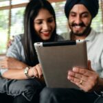 Joyful young Indian couple watching video on tablet and having fun