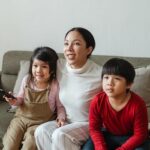 Happy young ethnic mother and little children watching TV on sofa