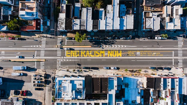 Overhead view of asphalt roadway with vehicles between building roofs and colorful title about racism