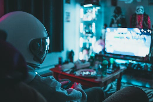 Side view of unrecognizable person in virtual reality helmet sitting on sofa and playing with gamepad in dark room
